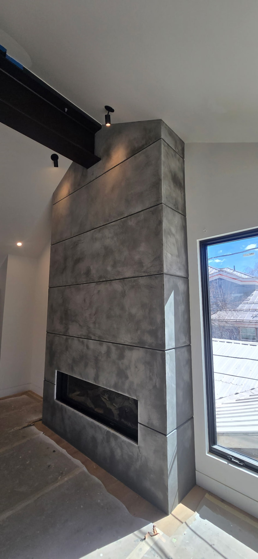 Full-height fireplace finished in charcoal micro-cement with cloudy movement